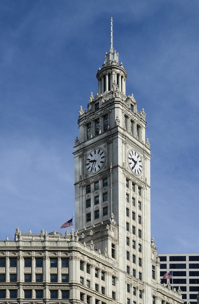 The white terra cotta clock tower of the Wrigley Building lit at dusk