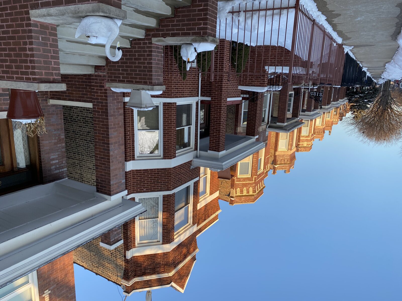 A row of near-identical brick Chicago two-flats in winter light, porches and stacked bays repeating down the street